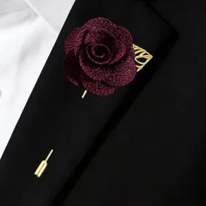 Vue rapprochée de la boutonnière rose bourgogne scintillante avec feuille et épingle dorées.