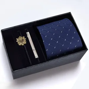 Detailed view of the blue patterned necktie, silver tie clip, and gold emblem in a gift box.