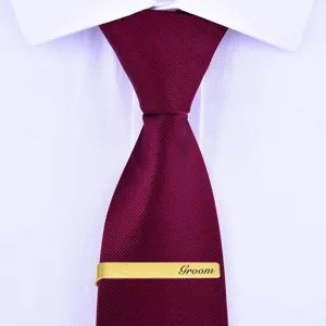 Detailed close-up of a gold stainless steel tie clip engraved with Groom on burgundy tie.