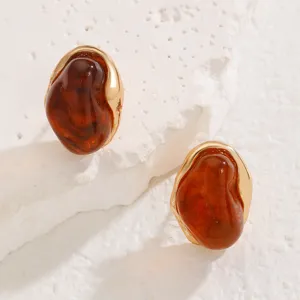 Close-up detail shot of vintage irregular amber resin earrings with elegant gold trim.