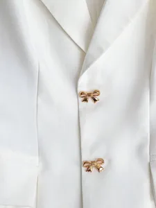 Detailaufnahme einer weißen Blazerweste mit eleganten goldenen Schleifenknöpfen, Mode.