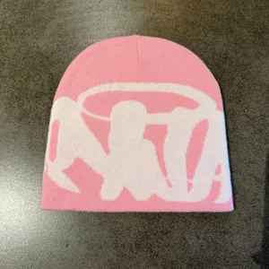 Close up of pink knitted beanie with white jacquard letter, cozy street style cold hat detail.