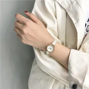 Detailweergave van een minimalistisch dameshorloge met witte leren band en gouden wijzerplaat.