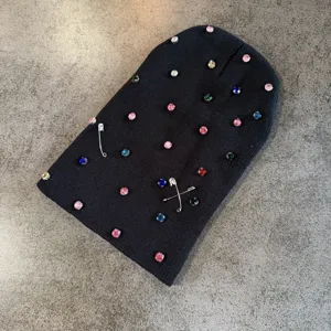 Modieuze zwarte gebreide muts met kleurrijke strass-steentjes en veiligheidsspelden.