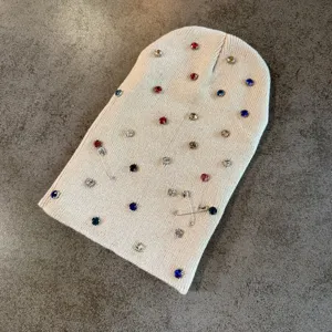 Close-up detail van beige gebreide muts versierd met kleurrijke strass-steentjes en veiligheidsspelden.