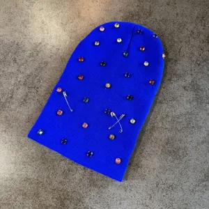 Gedetailleerd overzicht van een helderblauwe gebreide muts met kleurrijke strass-steentjes en speldjes.