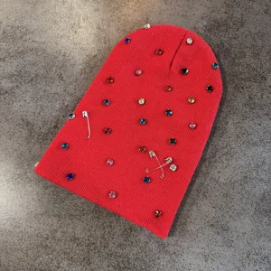Detailopname van een rode gebreide muts met kleurrijke strass-steentjes en spelden.
