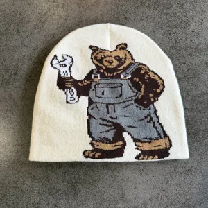 Vista dettagliata del berretto in maglia beige con un simpatico orso che tiene una chiave.