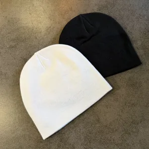 Detail shot of classic black and white knitted beanies, soft texture, warm winter headwear.