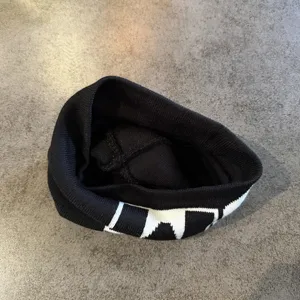 Gorro de punto negro con diseño jacquard de letras blancas, cálido y elegante para otoño e invierno.