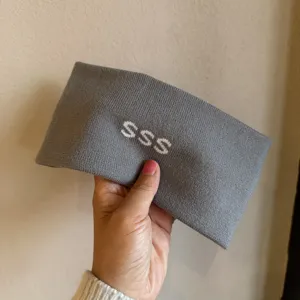 Detail shot of a wide grey knitted headband featuring white embroidered SSS letters closeup view.