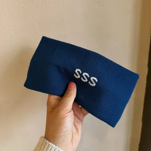 Close-up detail of the blue knitted headband featuring white SSS letter embroidery design.