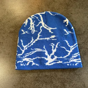 Bonnet en tricot bleu avec un motif jacquard de branches abstraites blanches pour streetwear.