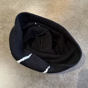 Vue detaillee du bonnet en tricot noir presentant un motif jacquard blanc contraste et tissu doux.