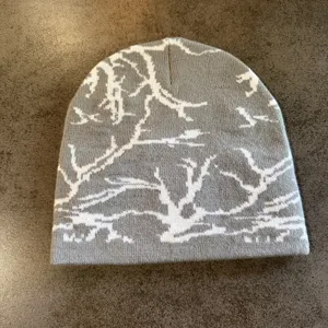 Gros plan détail du bonnet en tricot gris avec motif jacquard de branches d'arbres.