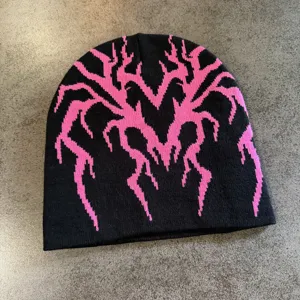 Vue détaillée du bonnet en tricot noir avec motif toile d'araignée cœur rose, chaud et stylé.