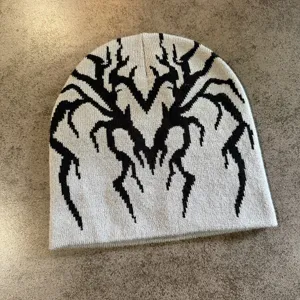 Gros plan du bonnet en tricot avec motif jacquard noir détaillé sur fond de tissu gris.
