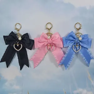 Detail view of pleated ribbon bow keychain with pearls and heart charms in black, pink, blue.