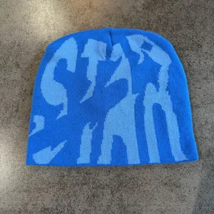 Blue knit beanie hat with bold stylized letter pattern, cozy hip-hop winter streetwear style.