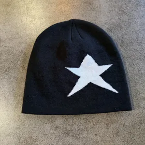 Close-up of black knit beanie with white star detail, casual winter streetwear fashion accessory.