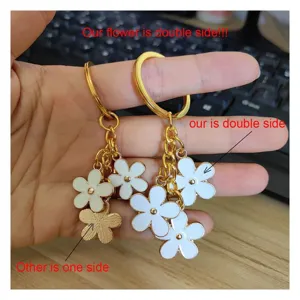 Primo piano dettaglio portachiavi dorato con ciondoli fiori in smalto bianco a doppia faccia.