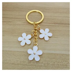 Dettaglio portachiavi fiore in smalto con tre ciondoli floreali bianchi e accessori oro.