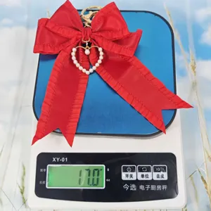 Red fabric ribbon bow keychain detail shot featuring pearl heart pendant and golden keyring.