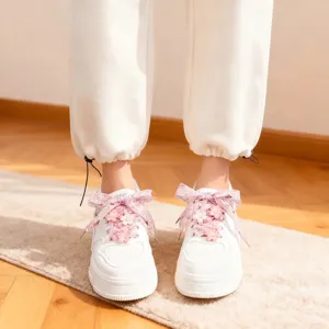 Detailed view of white sneakers featuring pink cherry blossom decorations and organza laces.