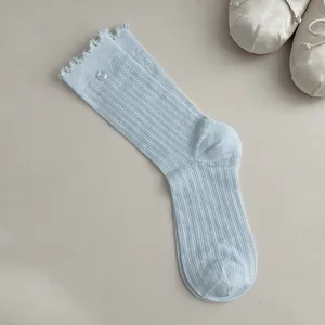 Detail view of light blue ribbed crew socks with cute flower button and ruffle cuff design.