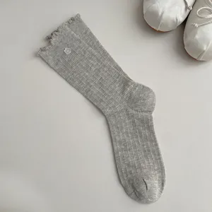 Detail view of grey ribbed mid-calf socks featuring lettuce ruffles and a cute flower button.