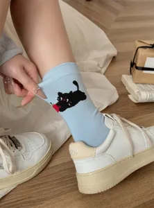 Detail shot of cute cartoon black cat and apple pattern on light blue cotton socks.