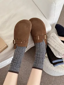Close-up of brown suede mule clogs paired with cozy knit grey slouch socks for autumn winter.