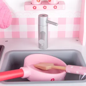 Wooden toy kitchen sink detail shot, featuring pink toy pan and wooden spatula accessories.