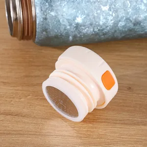 Détail de couvercle de tasse isotherme en titane, filtre à thé et bouton orange.