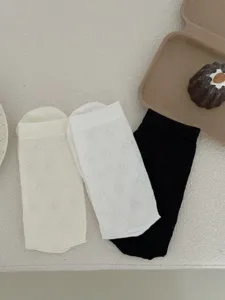 Close-up detail of thin breathable jacquard monogram socks in black white and beige knit design.