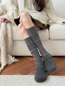 Detailed close-up of grey knitted hollow-out calf socks worn with cozy shoes on a warm sofa setting.