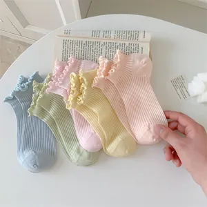 Close-up detail of pastel ruffled ankle socks in various soft colors on a white aesthetic table.