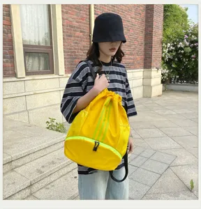 Nahaufnahme des gelben Kordelzug-Rucksacks mit grünen Streifen und Netztaschen draußen.