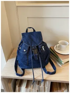 Vue détaillée du sac à dos en jean avec tissu bleu, fermeture à cordon et poches avant.