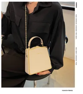 Detail view of an elegant white structured box handbag featuring a stylish gold chain strap.