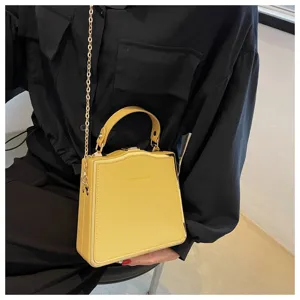 Detailed shot of yellow structured box bag with metal chain strap and top handle fashion accessory.