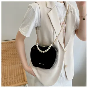 Close-up detail of stylish heart-shaped pearl chain crossbody bag worn by model.