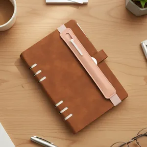 Leather notebook detail view, brown cover with pink elastic pen holder band on desk.