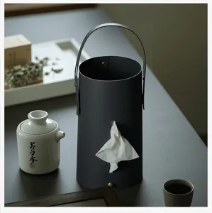 Detail shot of a dark gray leather cylindrical tissue holder with handle on a minimalist table.