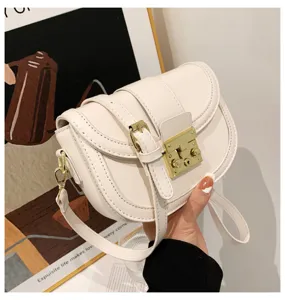 Detailed view of white saddle bag with golden lock and strap design, elegant fashion accessory.