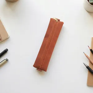 Detail view of a brown PU leather pencil pouch with golden zipper, flat lay desk scene setup.