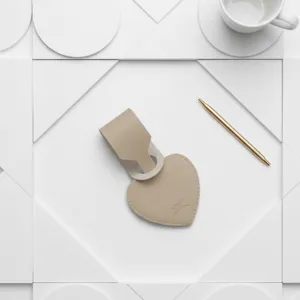 Primer plano de etiqueta de equipaje de cuero en forma de corazón beige con bolígrafo fondo blanco.