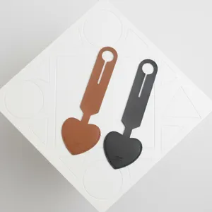 Detalle de etiqueta de equipaje de cuero en forma de corazon, marron y gris oscuro.