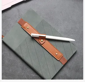 Primo piano di un taccuino verde minimalista con cinturino portapenna in pelle e penna bianca.