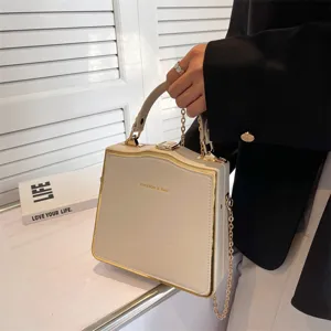 Chic beige structured box handbag with gold trim, top handle, and elegant chain strap.